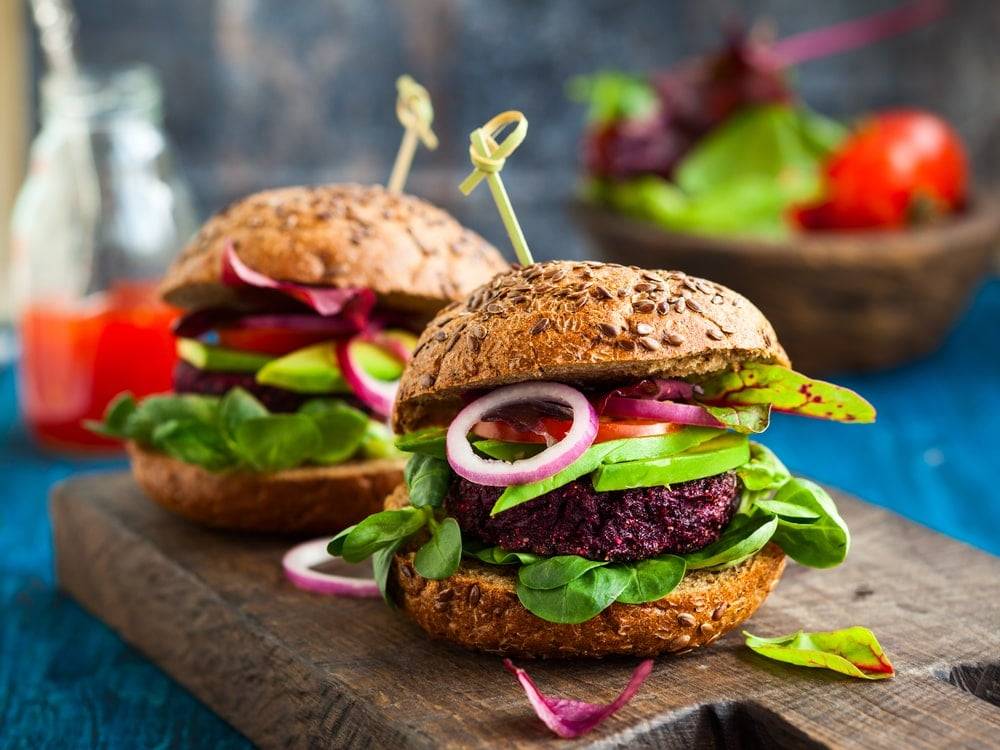 Two chunky beetroot burgers on a thick wooden chopping board