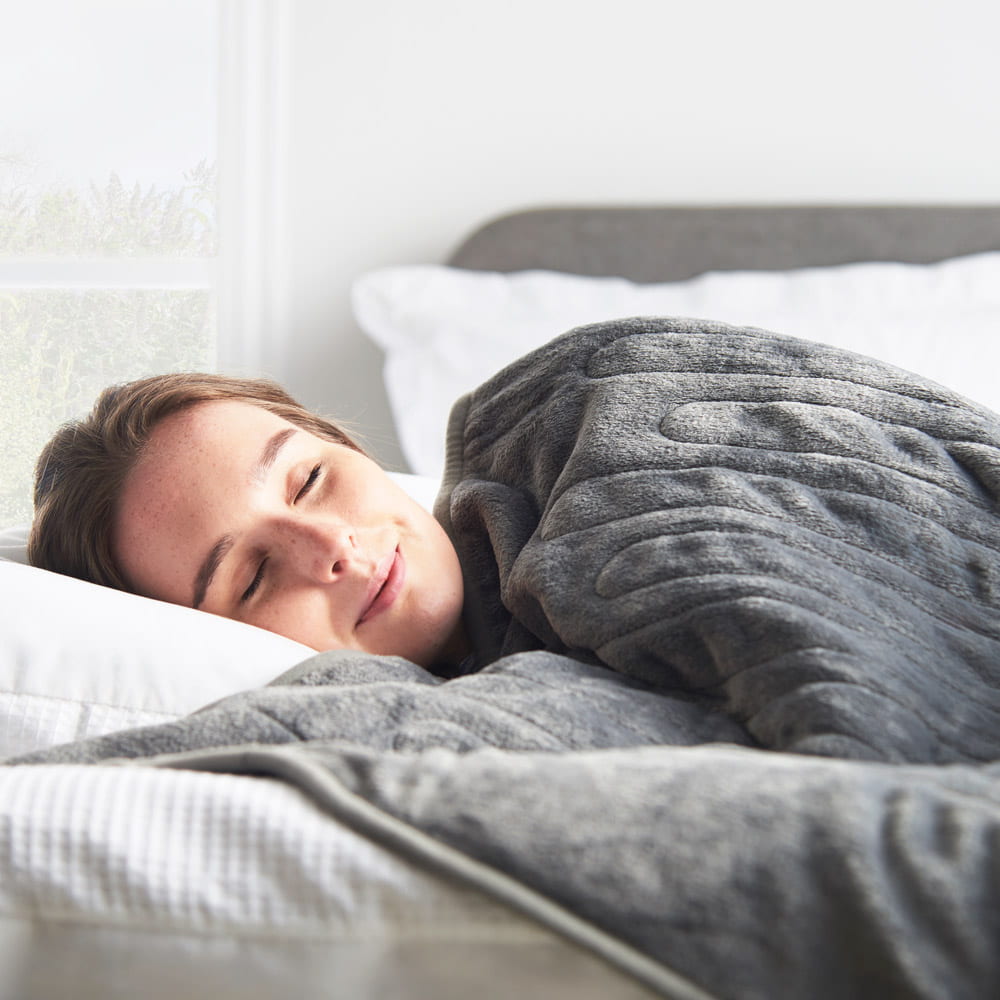 Girl sleeping under a grey Vonhaus heated throw