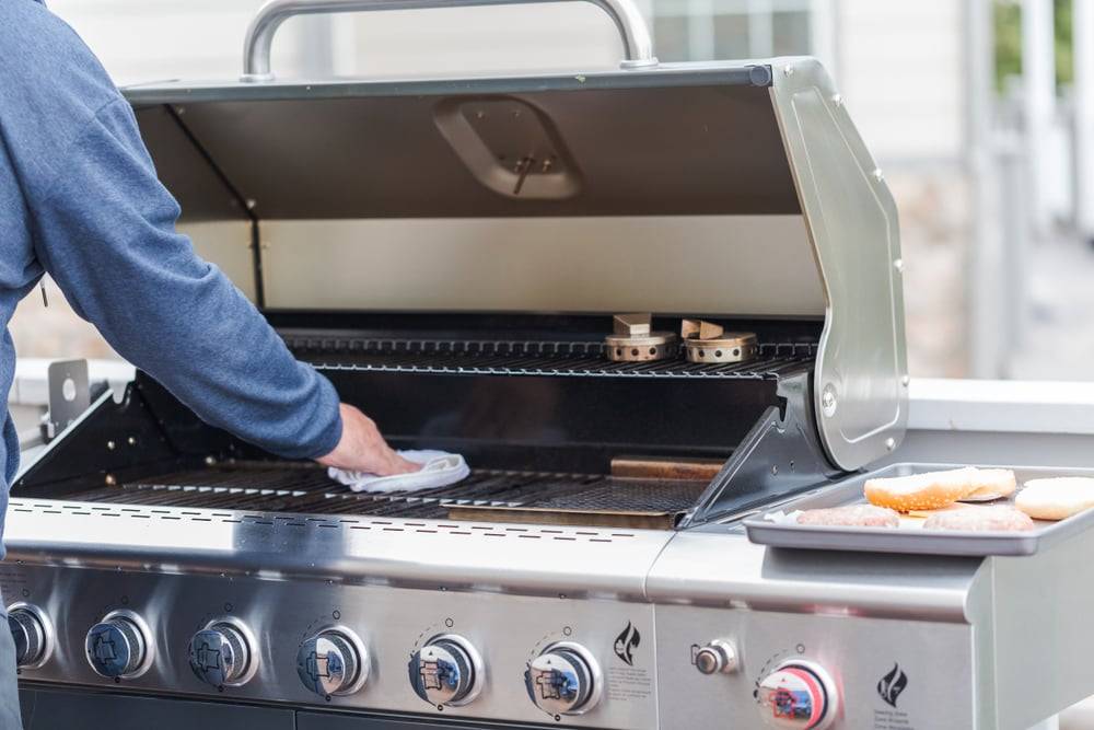 Man cleaning a large silver BBQ