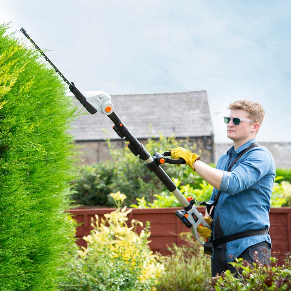 Man cutting hedge with pole hedge trimmer