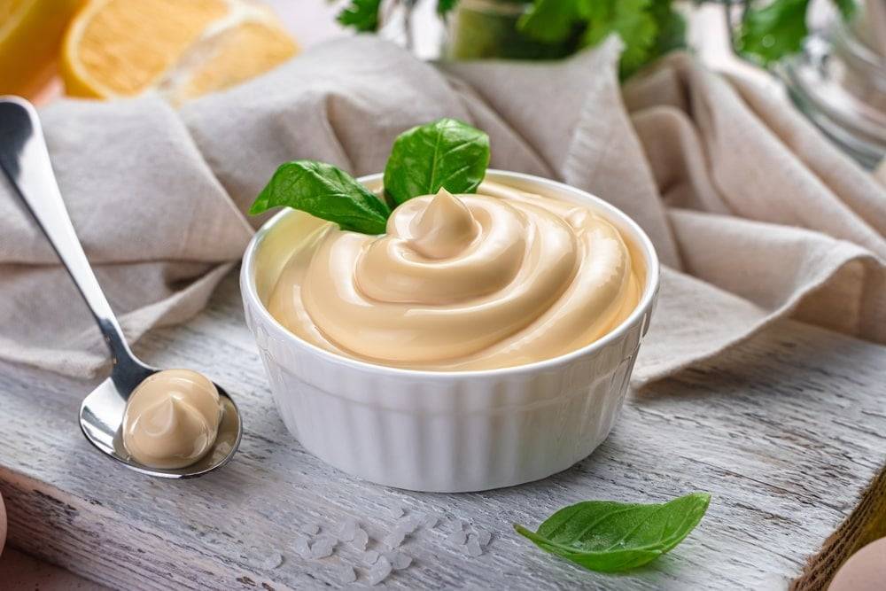 Creamy vegan mayo in small white dish on a wooden chopping board 