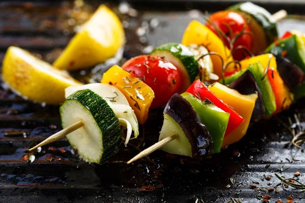 Seasoned vegetable kebabs on an on outdoor stone grill 