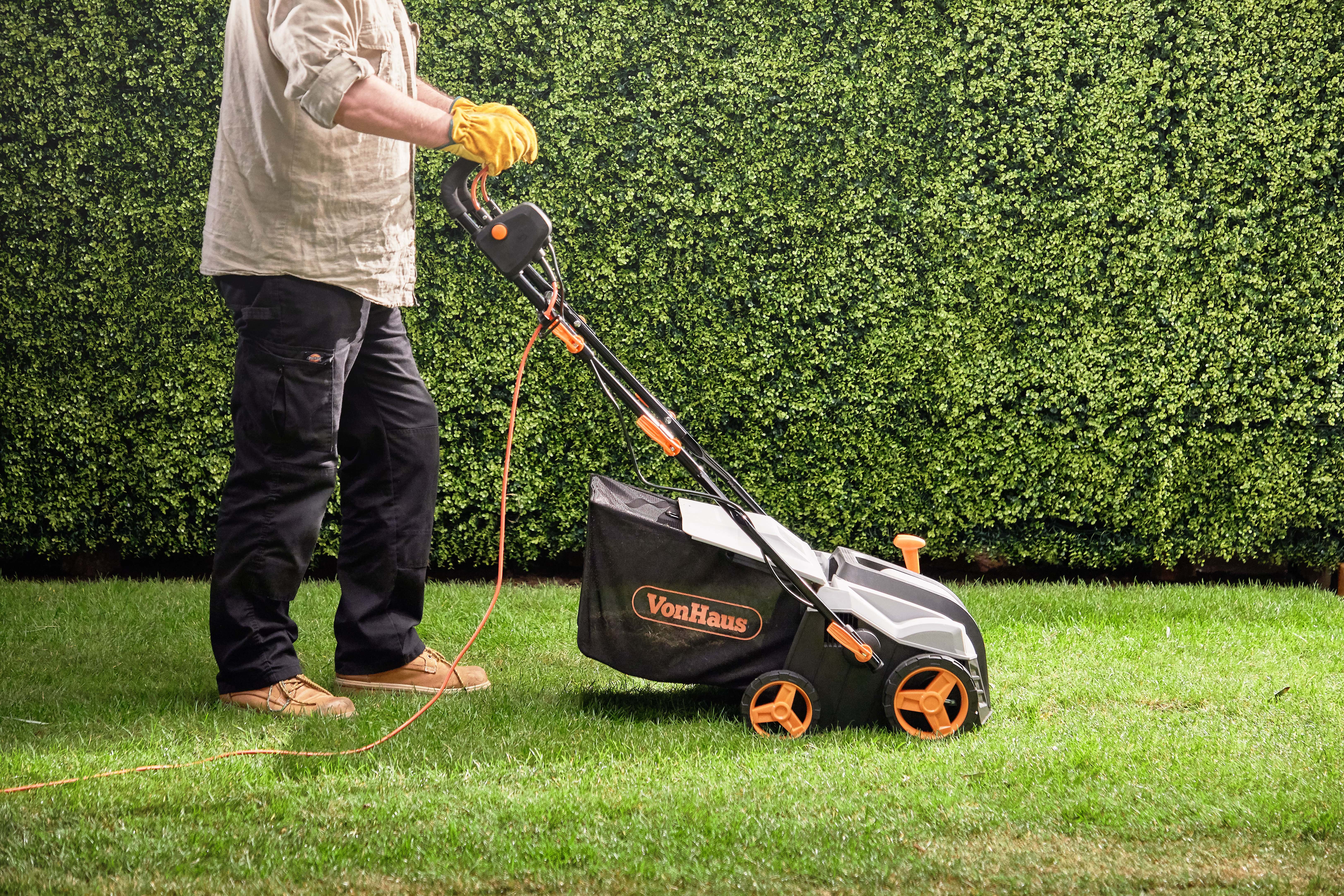 man pushing an electric scarifier on a lawn