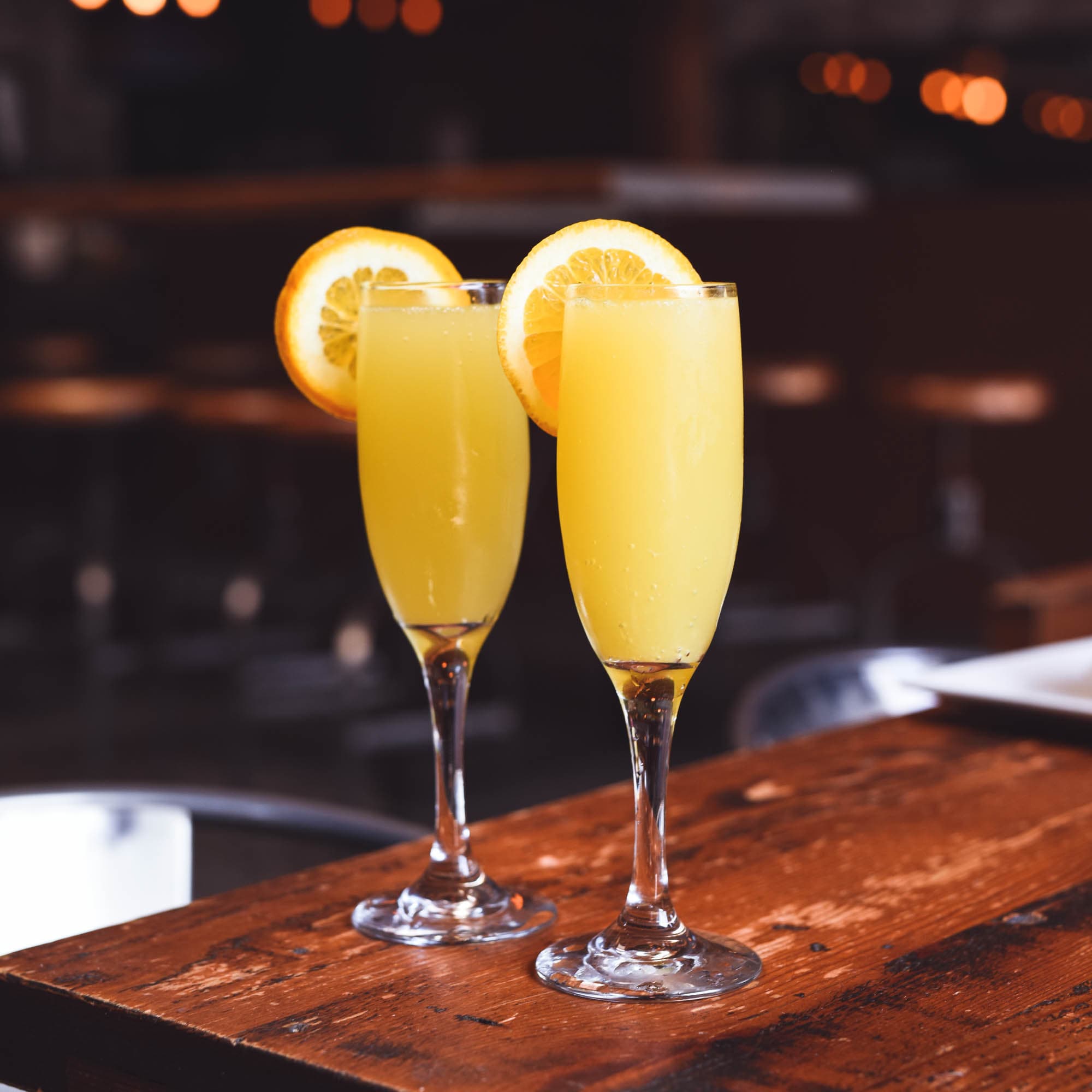 two prosecco mimosa cocktails with orange slice garnish on wood table