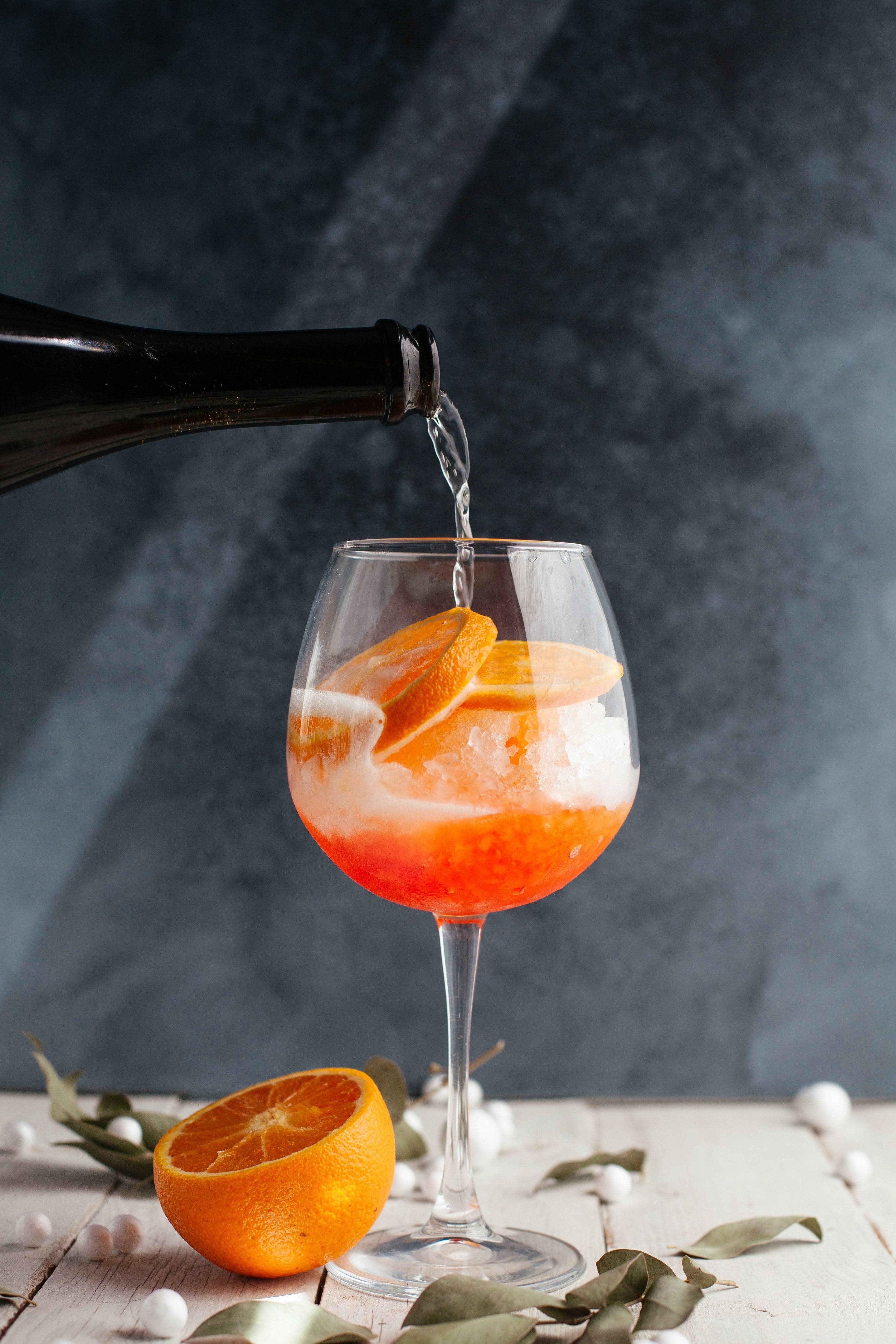 prosecco being poured into an aperol spritz cocktail with orange slice garnish